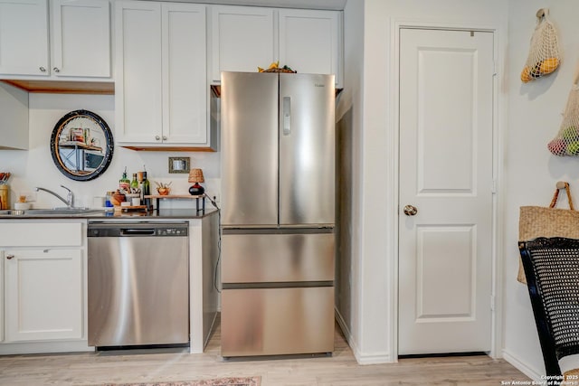 kitchen featuring appliances with stainless steel finishes, light wood-style floors, white cabinets, a sink, and baseboards