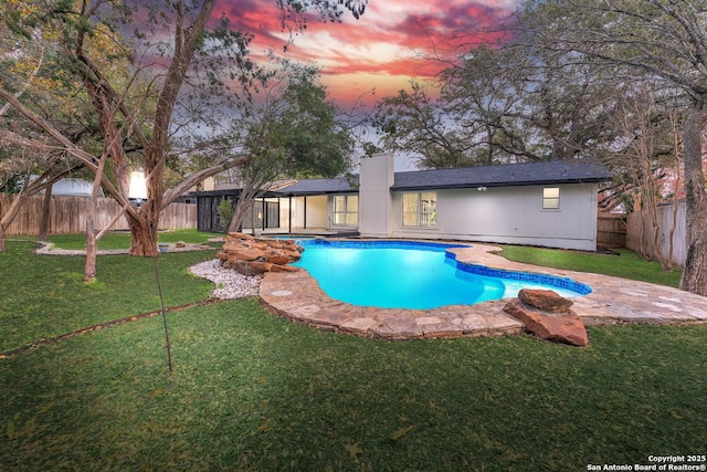 pool at dusk featuring a yard, a fenced backyard, and a fenced in pool