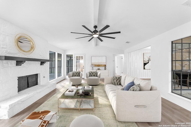 living area with lofted ceiling, visible vents, wood finished floors, and a stone fireplace