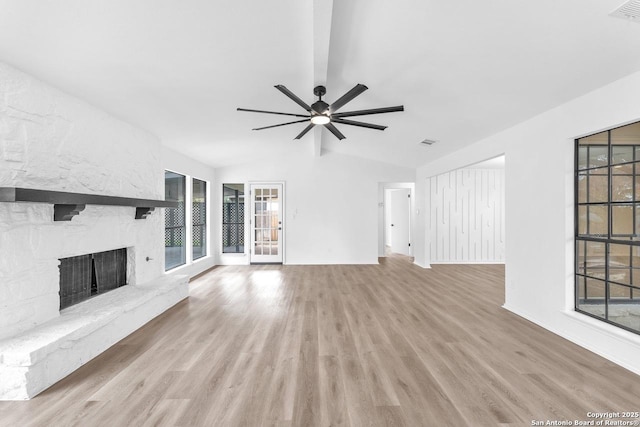 unfurnished living room with vaulted ceiling, a stone fireplace, wood finished floors, and visible vents