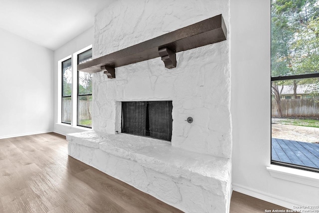 details featuring a stone fireplace, baseboards, and wood finished floors