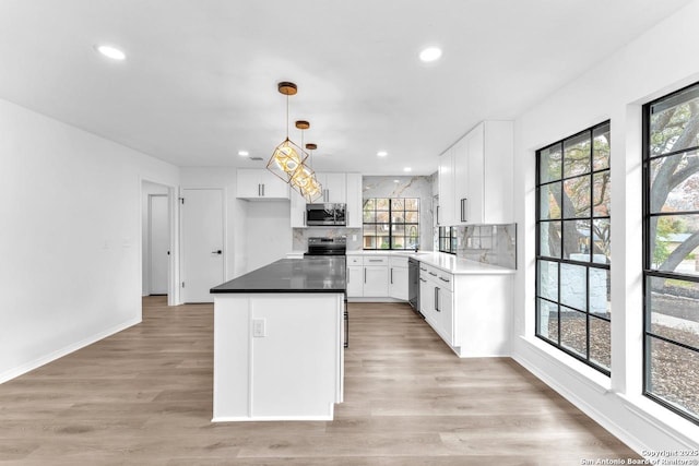 kitchen featuring stainless steel appliances, light wood-style flooring, backsplash, white cabinetry, and a kitchen island