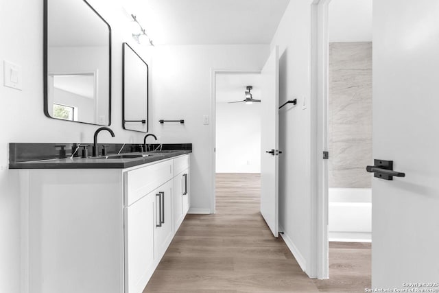 bathroom featuring double vanity, a sink, a bath, and wood finished floors