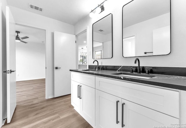 full bath with double vanity, visible vents, a sink, and wood finished floors