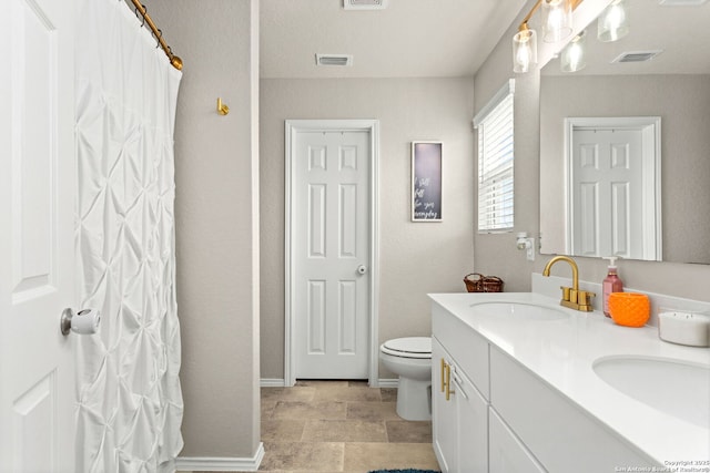 bathroom with toilet, double vanity, visible vents, and a sink