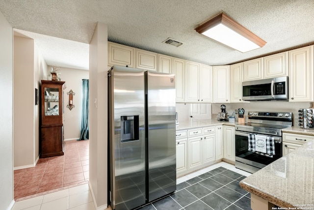 kitchen featuring a textured ceiling, dark tile patterned flooring, visible vents, appliances with stainless steel finishes, and light stone countertops