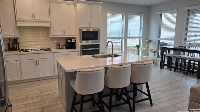 kitchen with stainless steel appliances, light countertops, light wood-type flooring, white cabinetry, and a sink