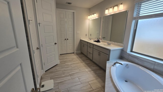 bathroom featuring double vanity, tiled tub, visible vents, and a sink