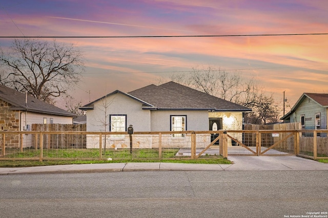 view of front of house featuring roof with shingles, a fenced front yard, a gate, and stucco siding