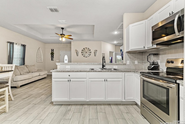 kitchen with a raised ceiling, appliances with stainless steel finishes, open floor plan, a peninsula, and a sink