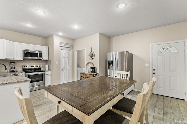 kitchen featuring white cabinets, appliances with stainless steel finishes, a sink, wood tiled floor, and backsplash