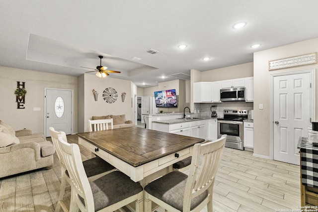 dining space featuring a tray ceiling, a ceiling fan, visible vents, and wood tiled floor