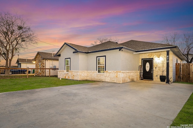 ranch-style house featuring stone siding, a lawn, fence, and concrete driveway