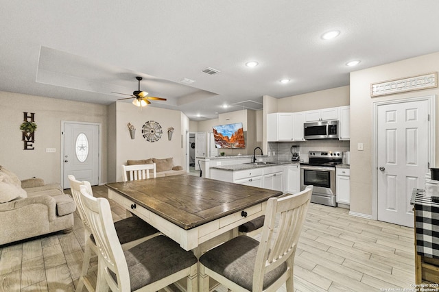 dining space featuring visible vents, a raised ceiling, ceiling fan, light wood-style flooring, and recessed lighting