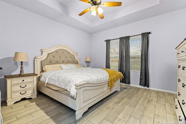 bedroom featuring light wood finished floors, baseboards, a raised ceiling, and a ceiling fan