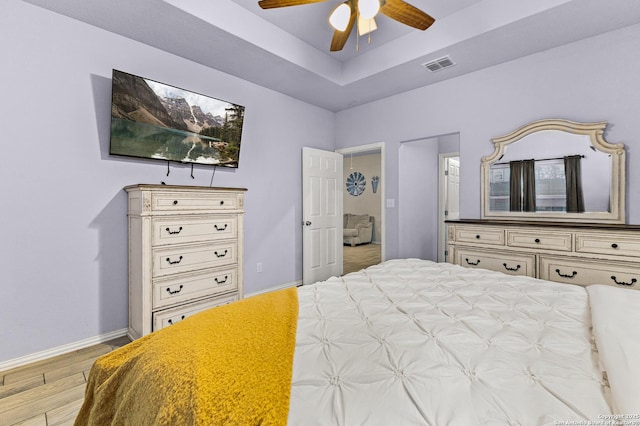 bedroom with baseboards, visible vents, a ceiling fan, wood finished floors, and a tray ceiling