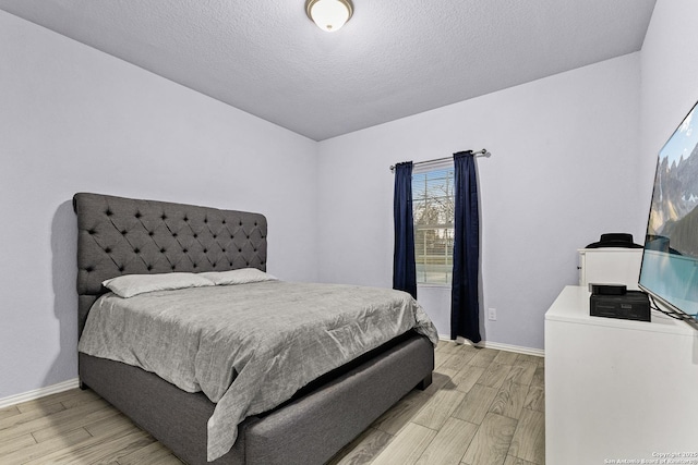 bedroom featuring a textured ceiling, light wood-style flooring, and baseboards