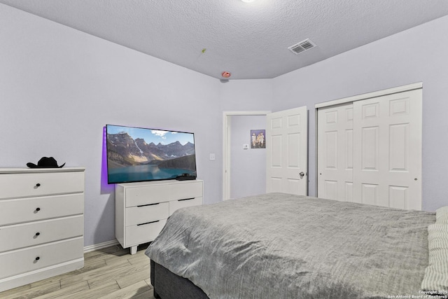 bedroom with a textured ceiling, a closet, light wood-type flooring, and visible vents