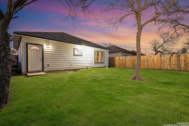 back of house at dusk featuring a lawn and fence