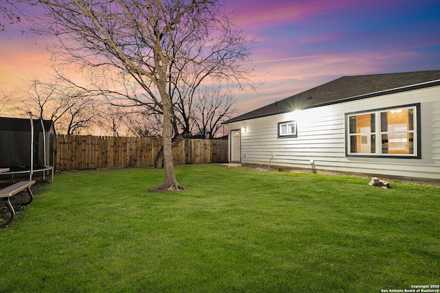 yard at dusk featuring a trampoline and fence