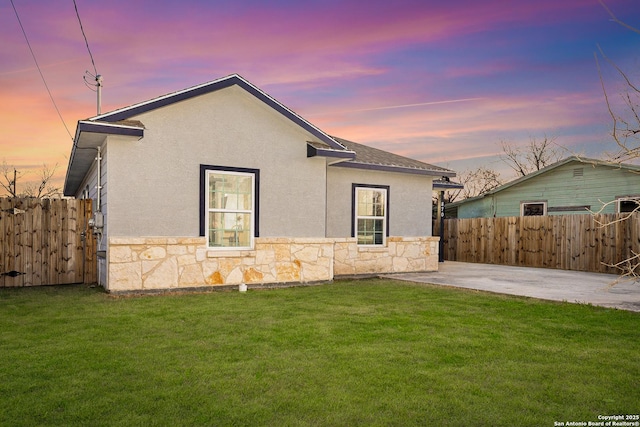 rear view of house featuring stone siding, fence, and a lawn