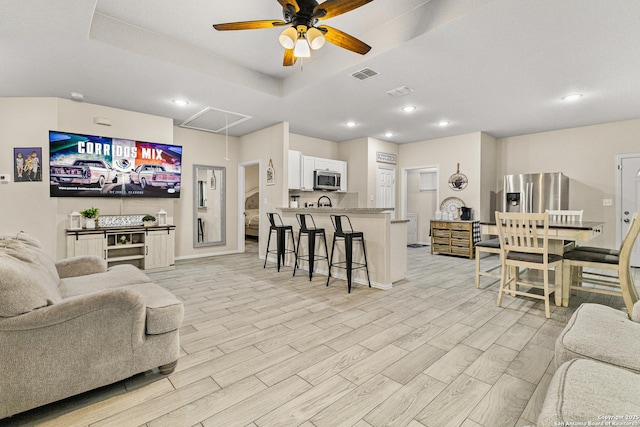 living room with wood finish floors, a raised ceiling, visible vents, attic access, and a ceiling fan