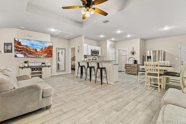 living area featuring a raised ceiling, visible vents, attic access, wood tiled floor, and ceiling fan