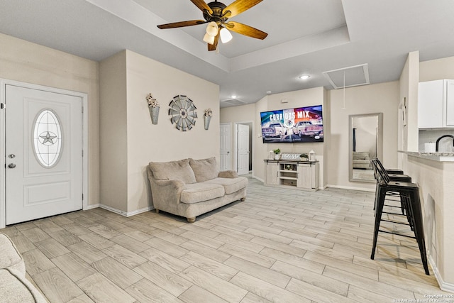 living area with a tray ceiling, attic access, a ceiling fan, wood tiled floor, and baseboards