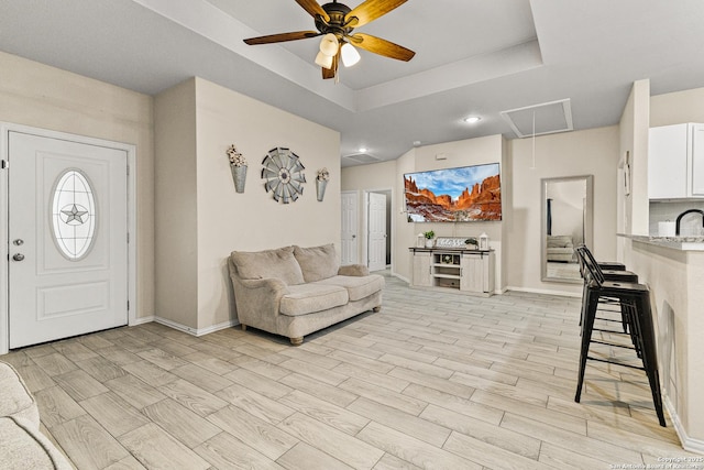 living room featuring attic access, a tray ceiling, baseboards, and wood finish floors