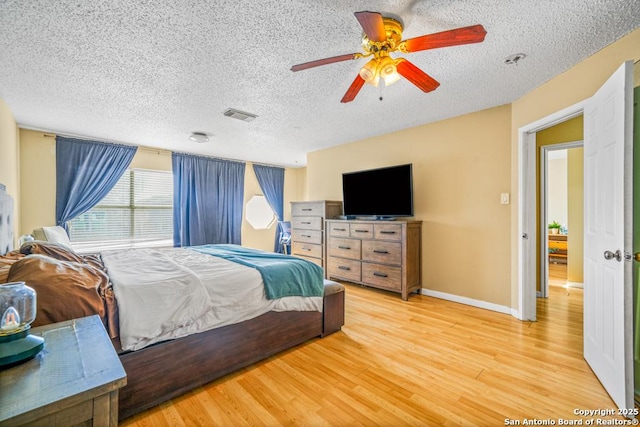 bedroom featuring baseboards, visible vents, a ceiling fan, wood finished floors, and a textured ceiling