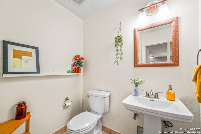 half bathroom with visible vents, toilet, a sink, a textured ceiling, and baseboards