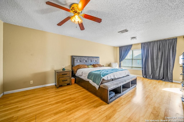 bedroom with a textured ceiling, wood finished floors, a ceiling fan, visible vents, and baseboards