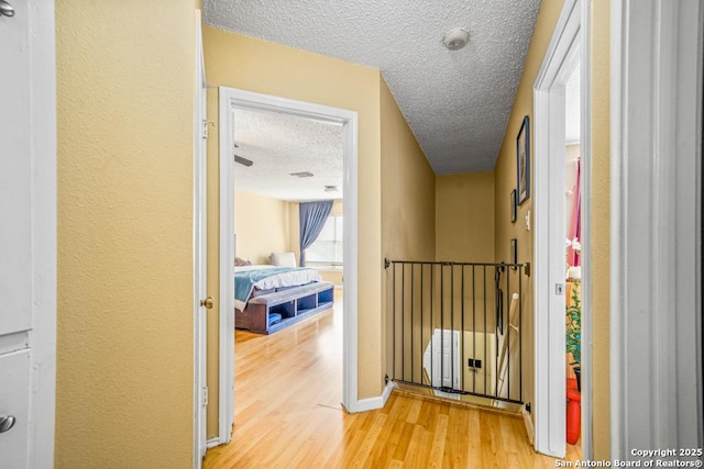 corridor featuring a textured ceiling, light wood finished floors, an upstairs landing, and baseboards