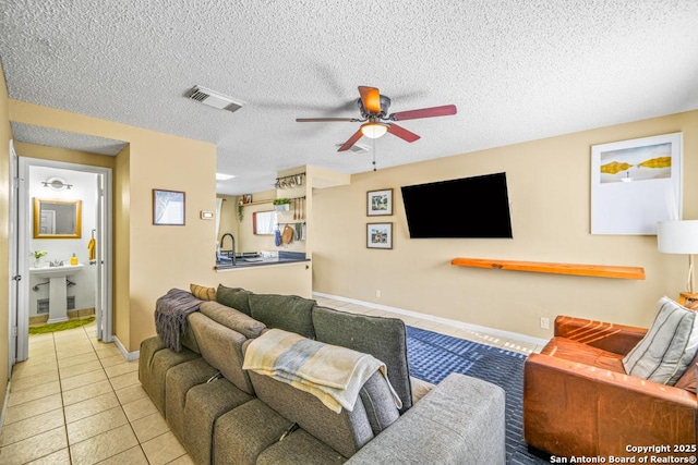 tiled living area featuring visible vents, ceiling fan, a textured ceiling, a sink, and baseboards