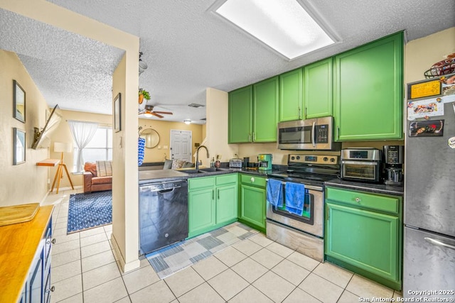 kitchen with light tile patterned floors, dark countertops, appliances with stainless steel finishes, a sink, and green cabinetry