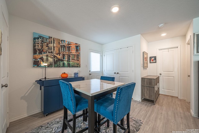 dining room featuring a textured ceiling, light wood-type flooring, and baseboards