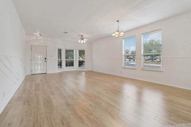 unfurnished living room featuring a wealth of natural light, visible vents, light wood-style flooring, and ceiling fan with notable chandelier