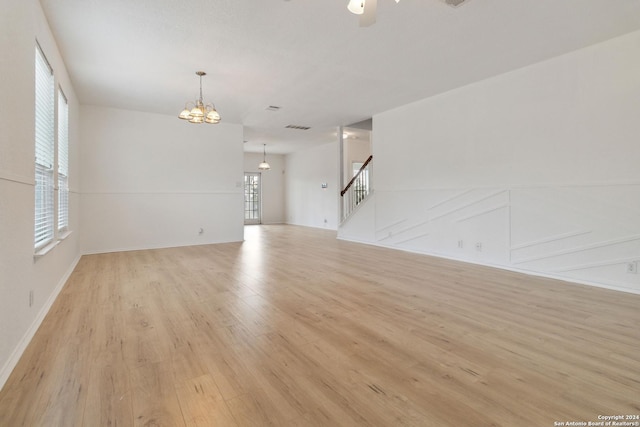 unfurnished living room with ceiling fan with notable chandelier, light wood finished floors, stairway, and visible vents