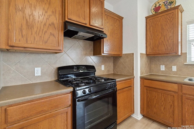 kitchen with brown cabinets, backsplash, black gas stove, and under cabinet range hood