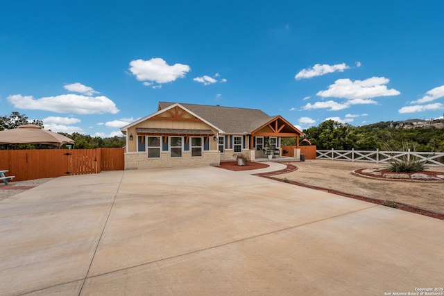 view of front of house featuring stone siding, a gate, a patio, and fence