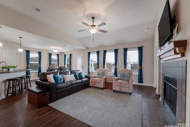 living area with dark wood-style floors, visible vents, vaulted ceiling, a tile fireplace, and baseboards