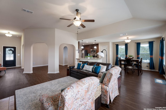 living area with arched walkways, dark wood-style flooring, visible vents, a ceiling fan, and vaulted ceiling