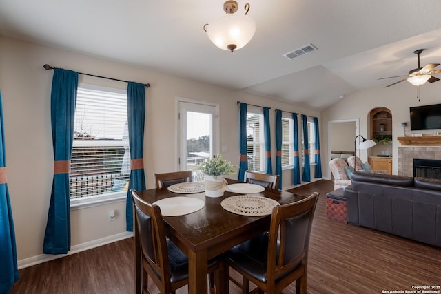 dining space featuring lofted ceiling, wood finished floors, visible vents, baseboards, and a tiled fireplace