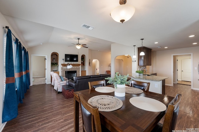 dining area with arched walkways, dark wood-style flooring, visible vents, a ceiling fan, and vaulted ceiling