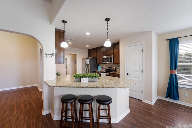 kitchen with appliances with stainless steel finishes, arched walkways, dark wood finished floors, and dark brown cabinetry