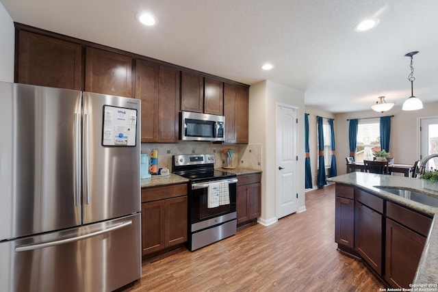 kitchen with appliances with stainless steel finishes, a sink, light stone countertops, light wood-type flooring, and backsplash