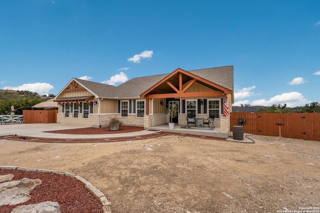 craftsman-style house featuring stone siding, a gate, fence, and cooling unit