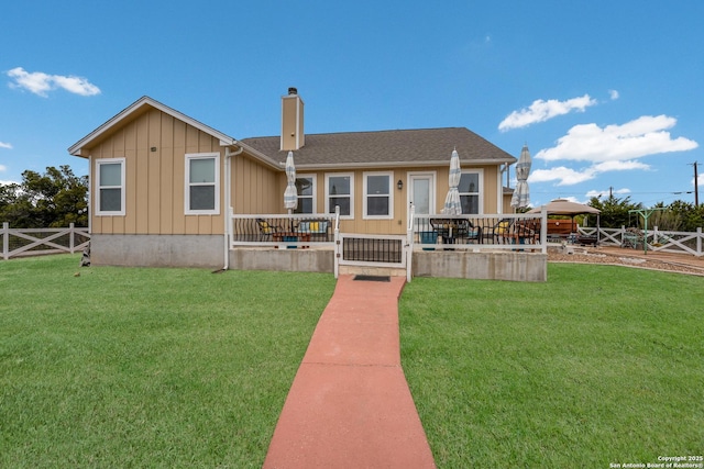 view of front of house featuring a front lawn, board and batten siding, a chimney, and fence