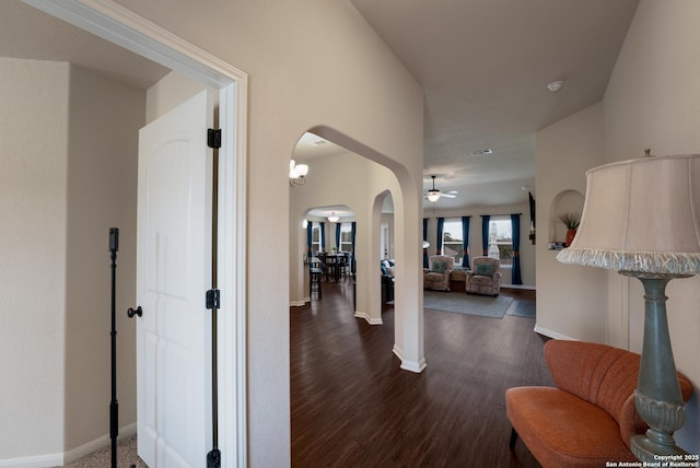 hallway featuring arched walkways, dark wood finished floors, and baseboards