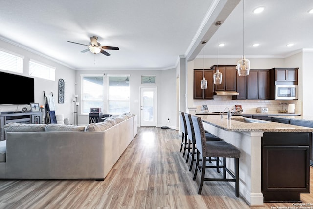 kitchen with a sink, open floor plan, dark brown cabinets, stainless steel microwave, and a kitchen bar